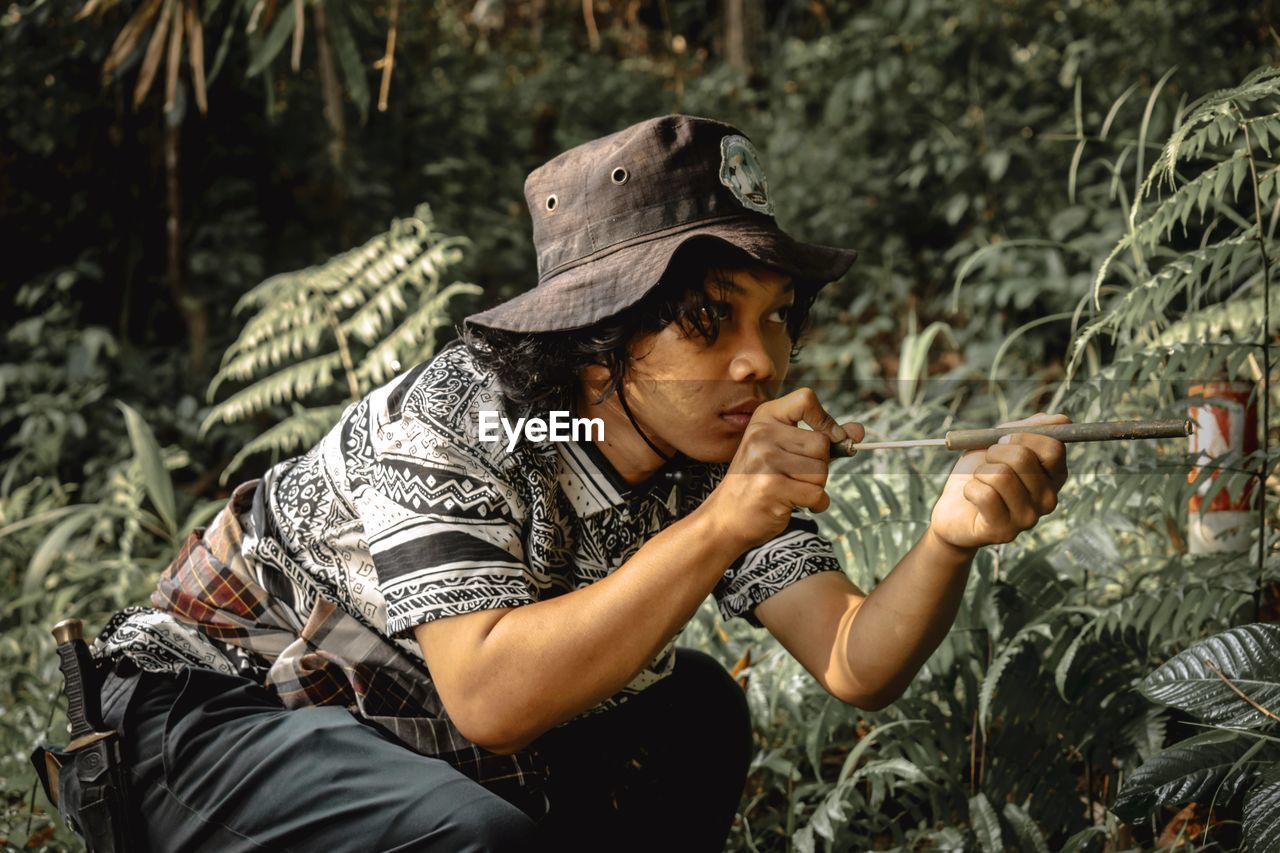 Young man wearing hat holding toy against plants in forest