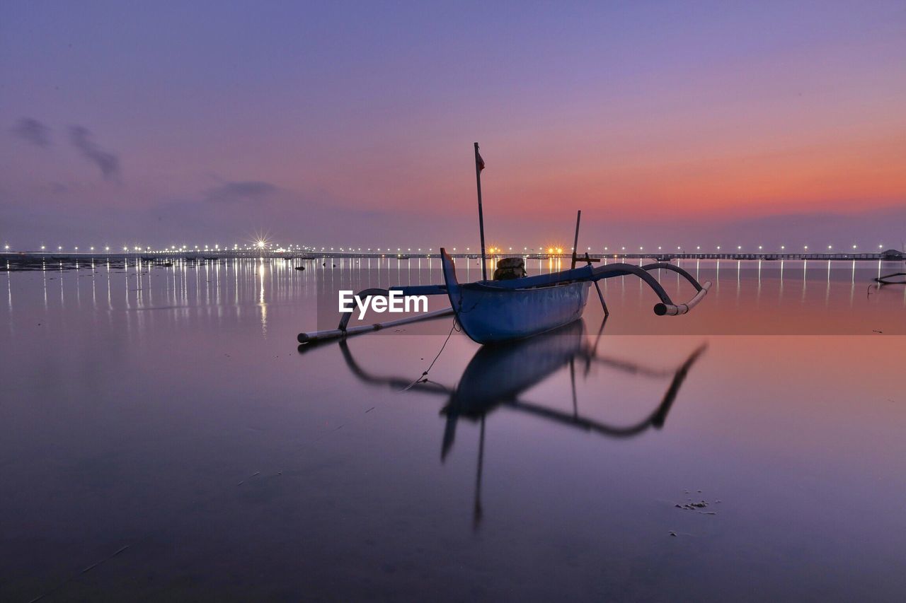 Outrigger boat at beach against sky during sunset