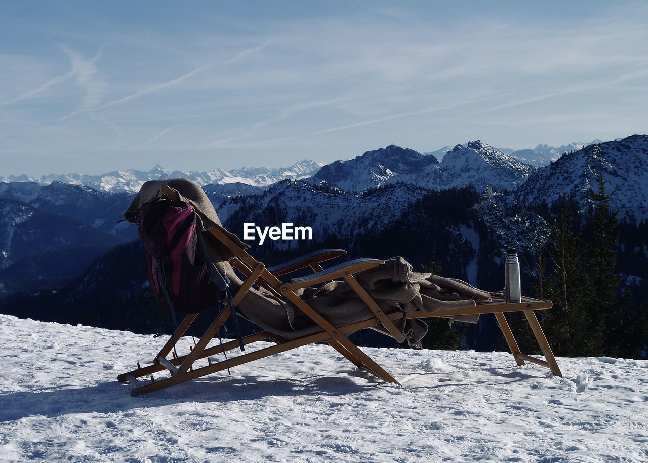 View of deck chair on snow covered land against sky