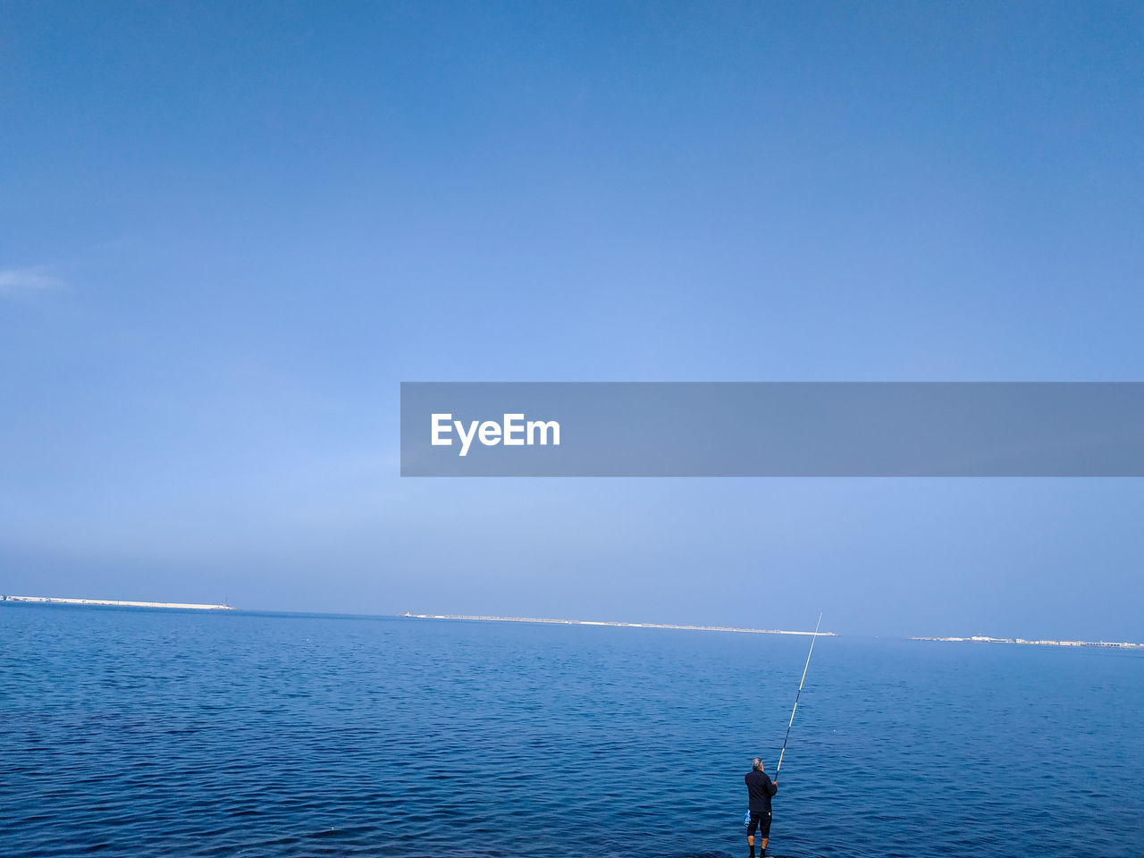 Man fishing in sea against blue sky