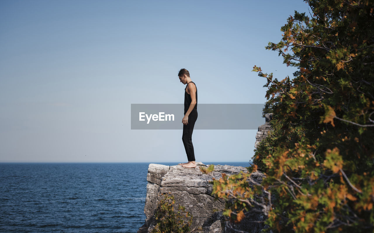 Full length of hiker standing on cliff against sea and clear sky at bruce peninsula national park