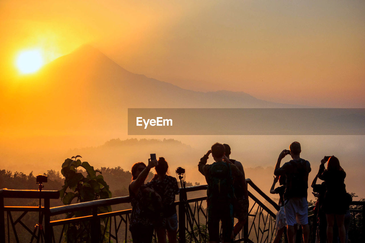 People photographing sunset from observation point at mountain