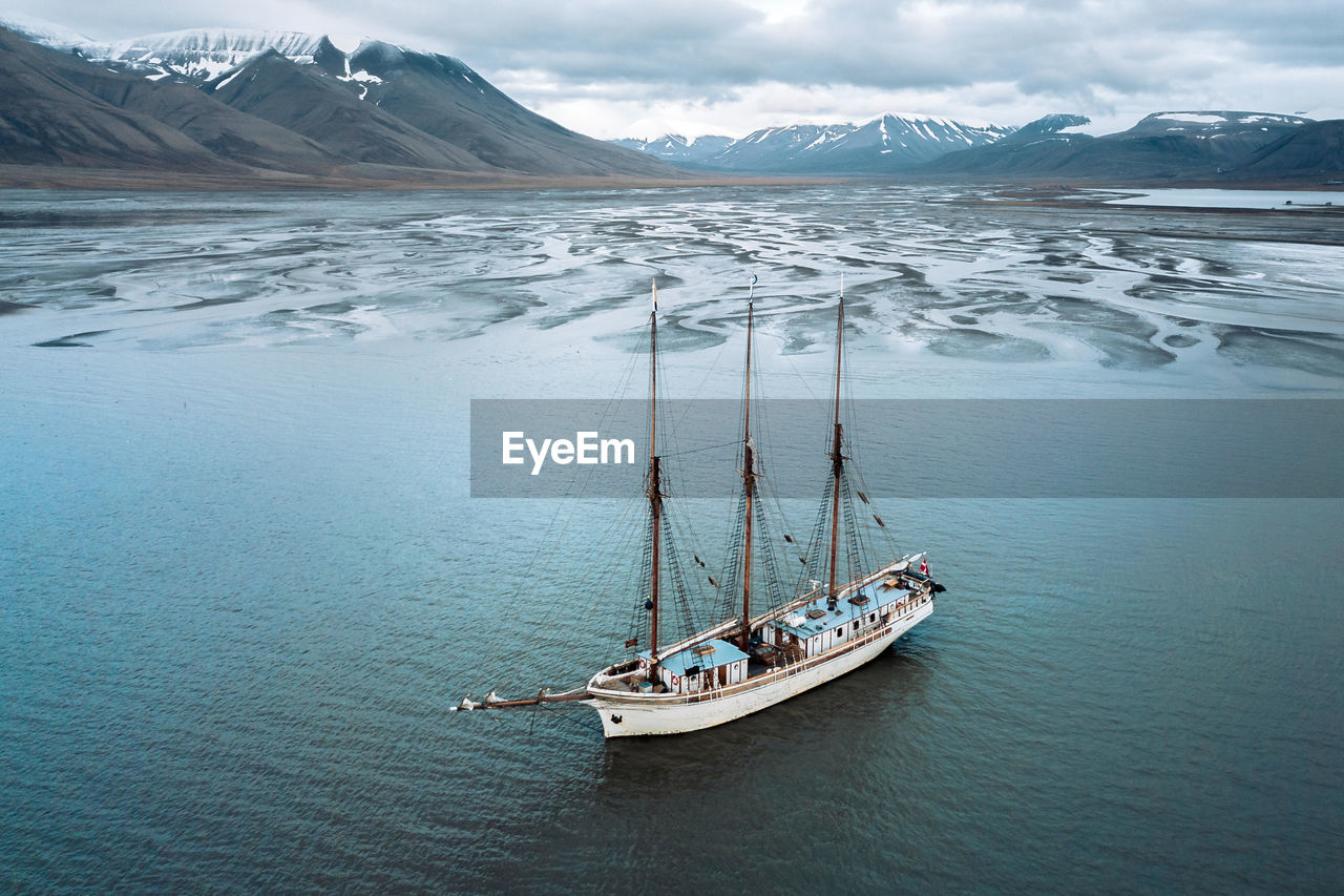 Boat moored in sea against mountains during winter