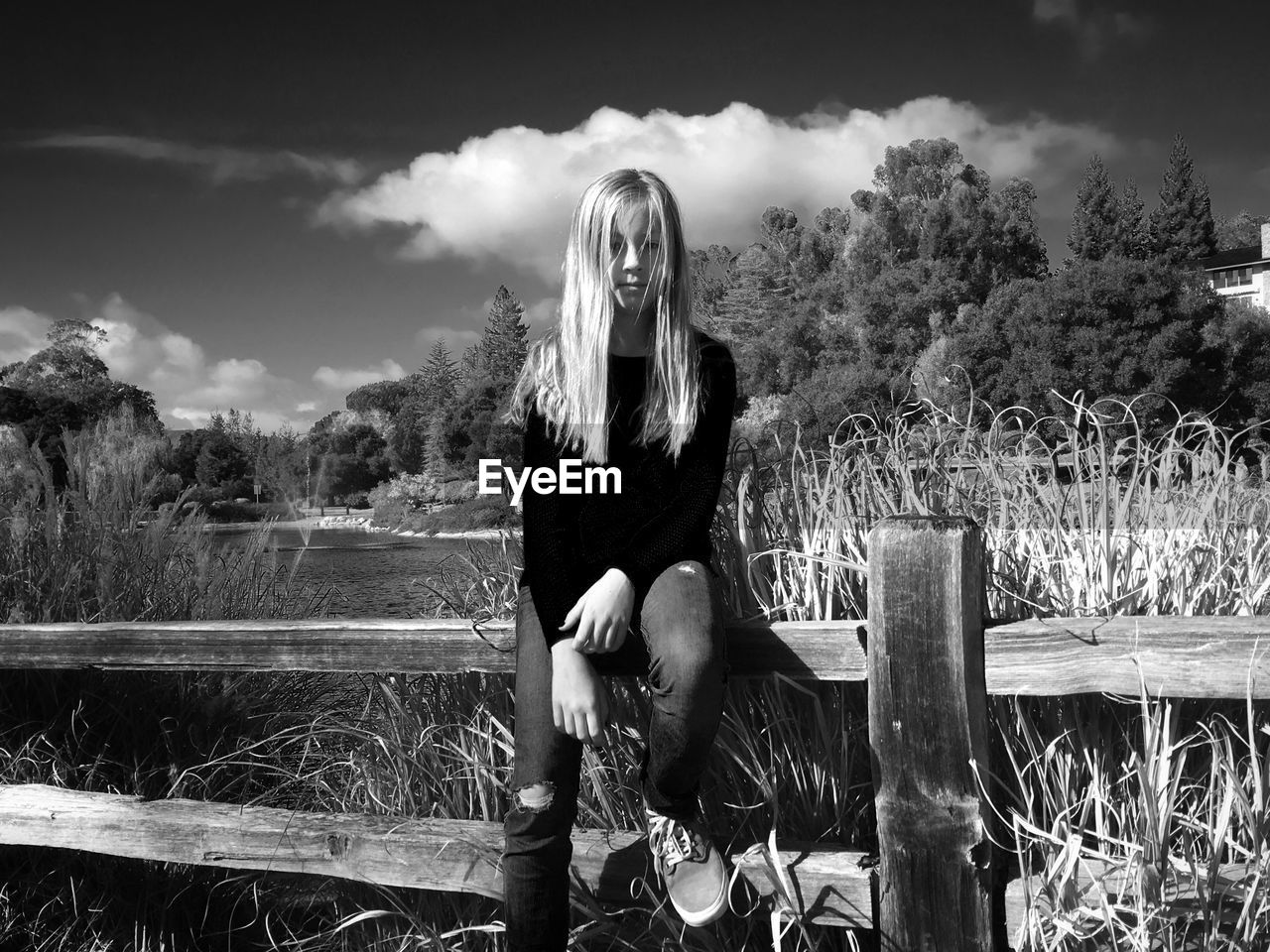 Girl sitting on railing against trees