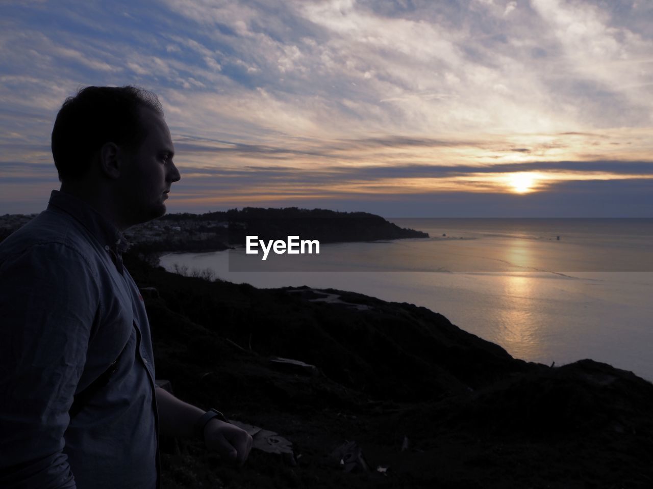 Side view of man standing at observation point against sea during sunset