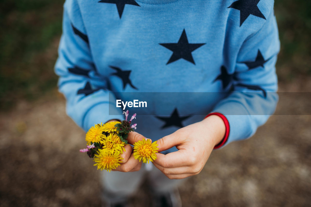 Close up of boy holding yellow flowers outside on a cold day in spring