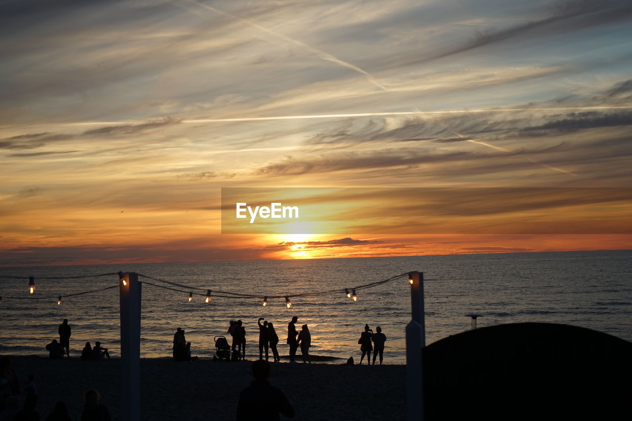 Silhouette people on beach against sky during sunset