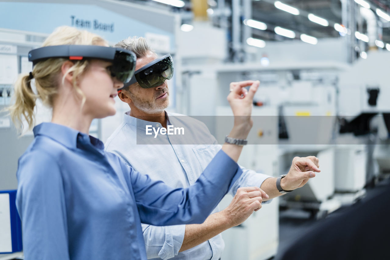 Coworkers discussing and using augmented reality eyeglasses in factory