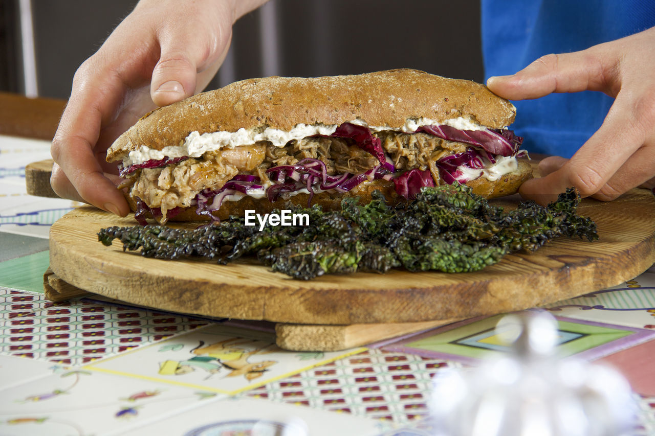 Two male hands taking pulled pork sandwich with vegetables and black cabbage chips 