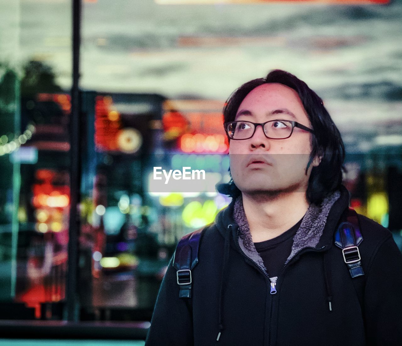 Portrait of young asian man in eyeglasses standing outside in city at night