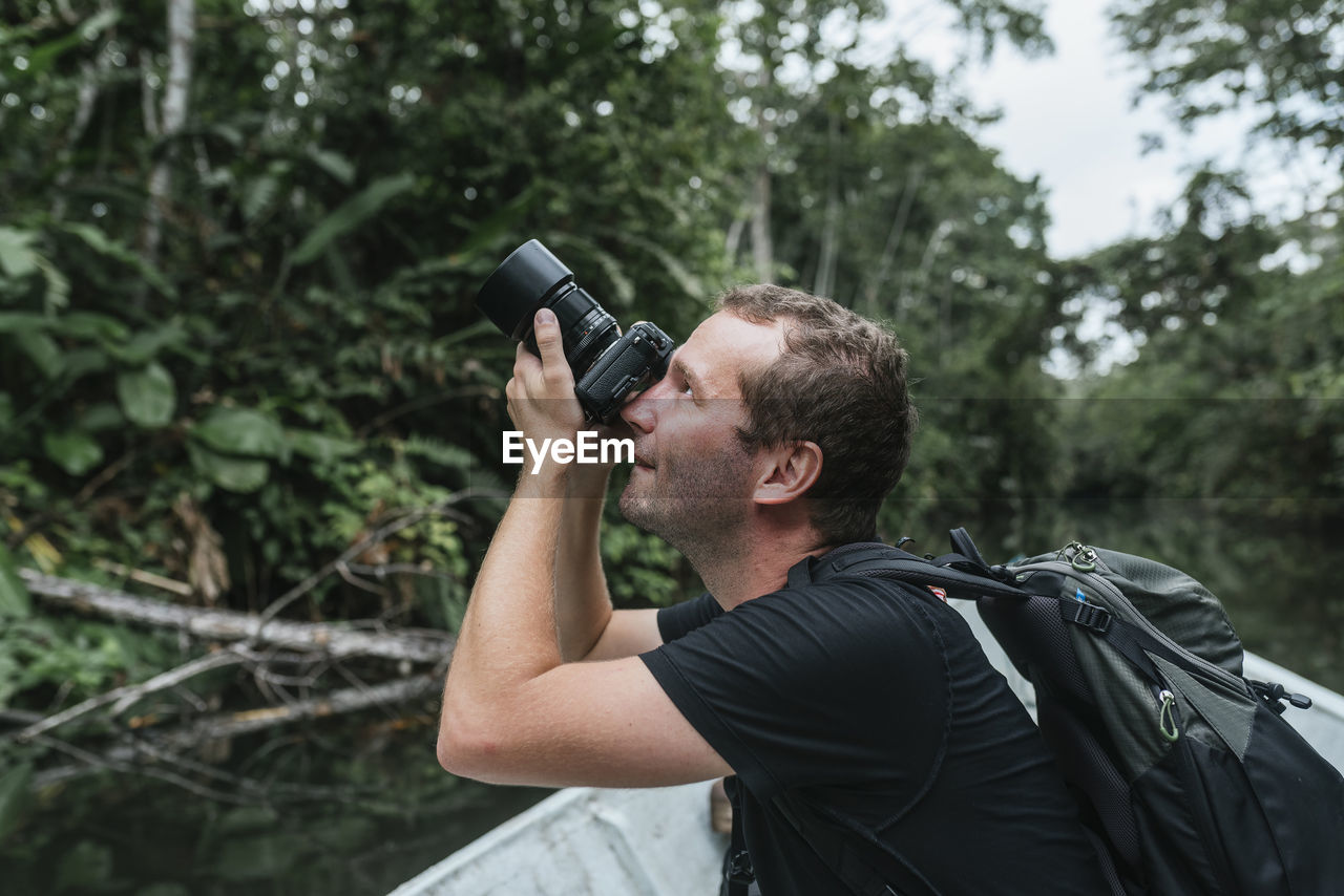 Male backpacker photographing nature from canoe at napo river, ecuador