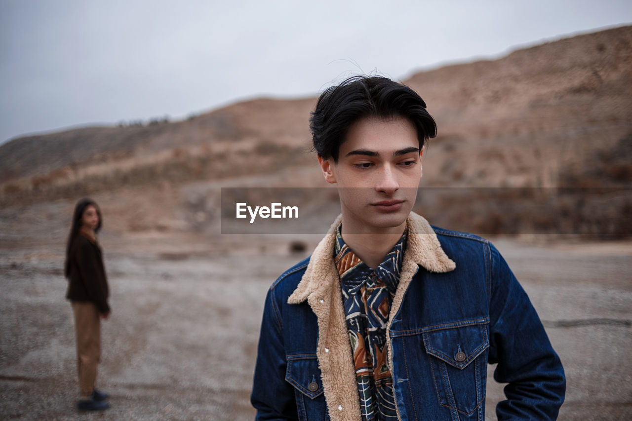 PORTRAIT OF YOUNG COUPLE STANDING ON LAND AGAINST SKY