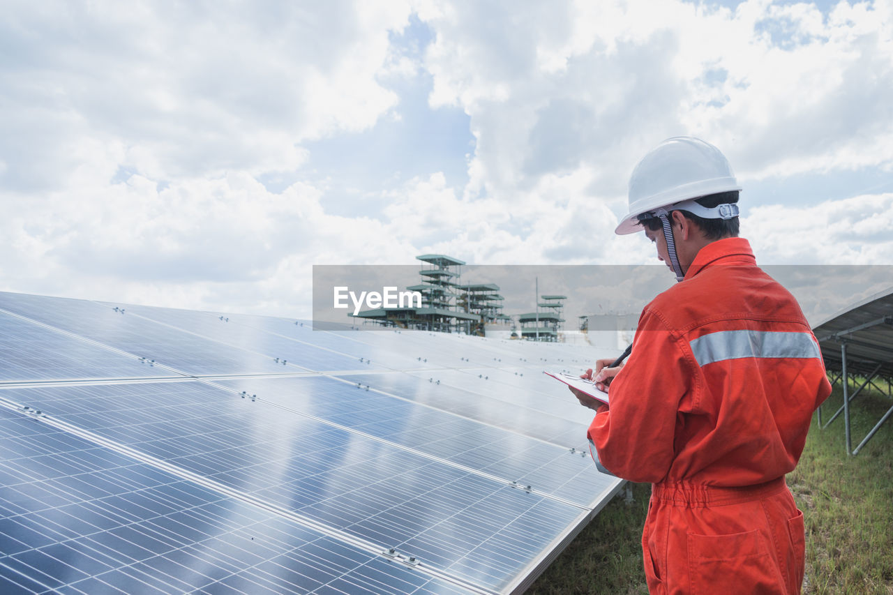 Engineer standing amidst solar panel against cloudy sky