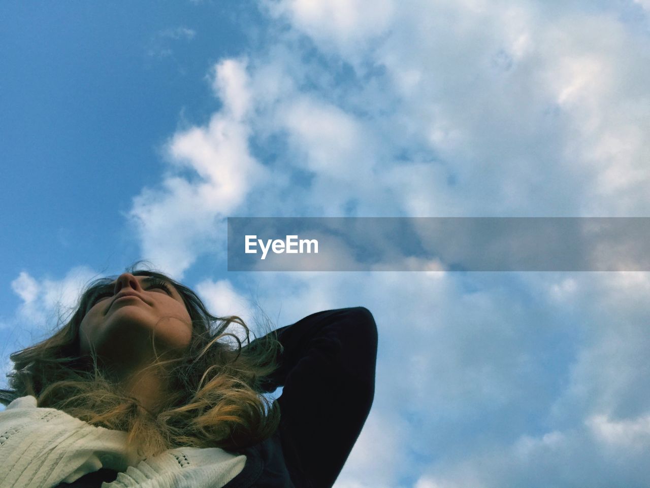 LOW ANGLE VIEW OF WOMAN AGAINST CLOUDY SKY