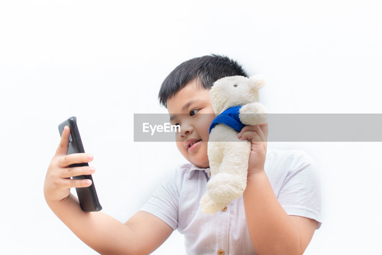 Boy holding toy while taking selfie against white background