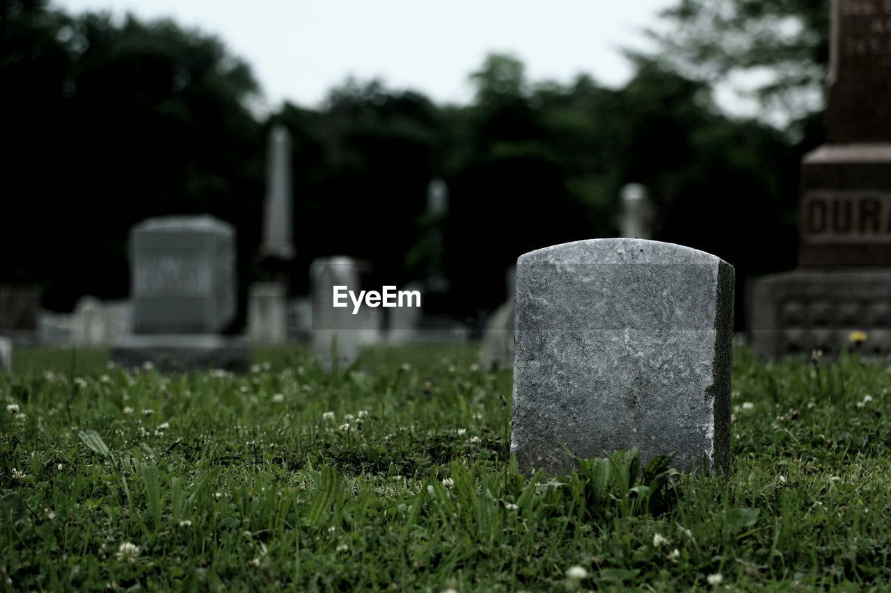 Tombstones on grassy field in cemetery against sky