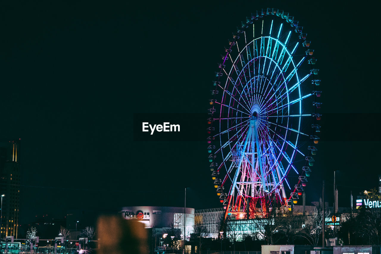 LOW ANGLE VIEW OF ILLUMINATED FERRIS WHEEL AGAINST SKY IN CITY
