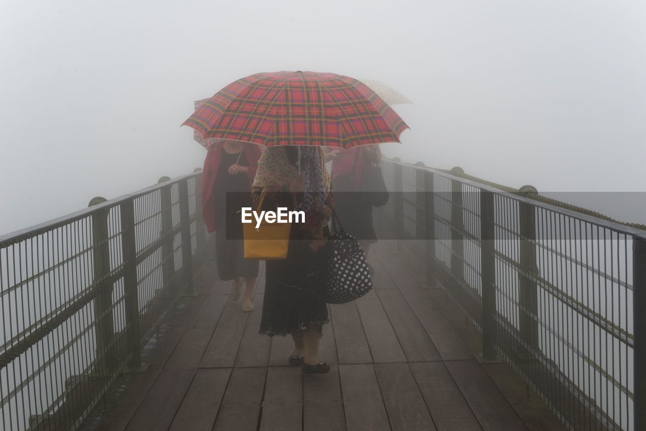 Women with umbrellas walking on footbridge during foggy weather