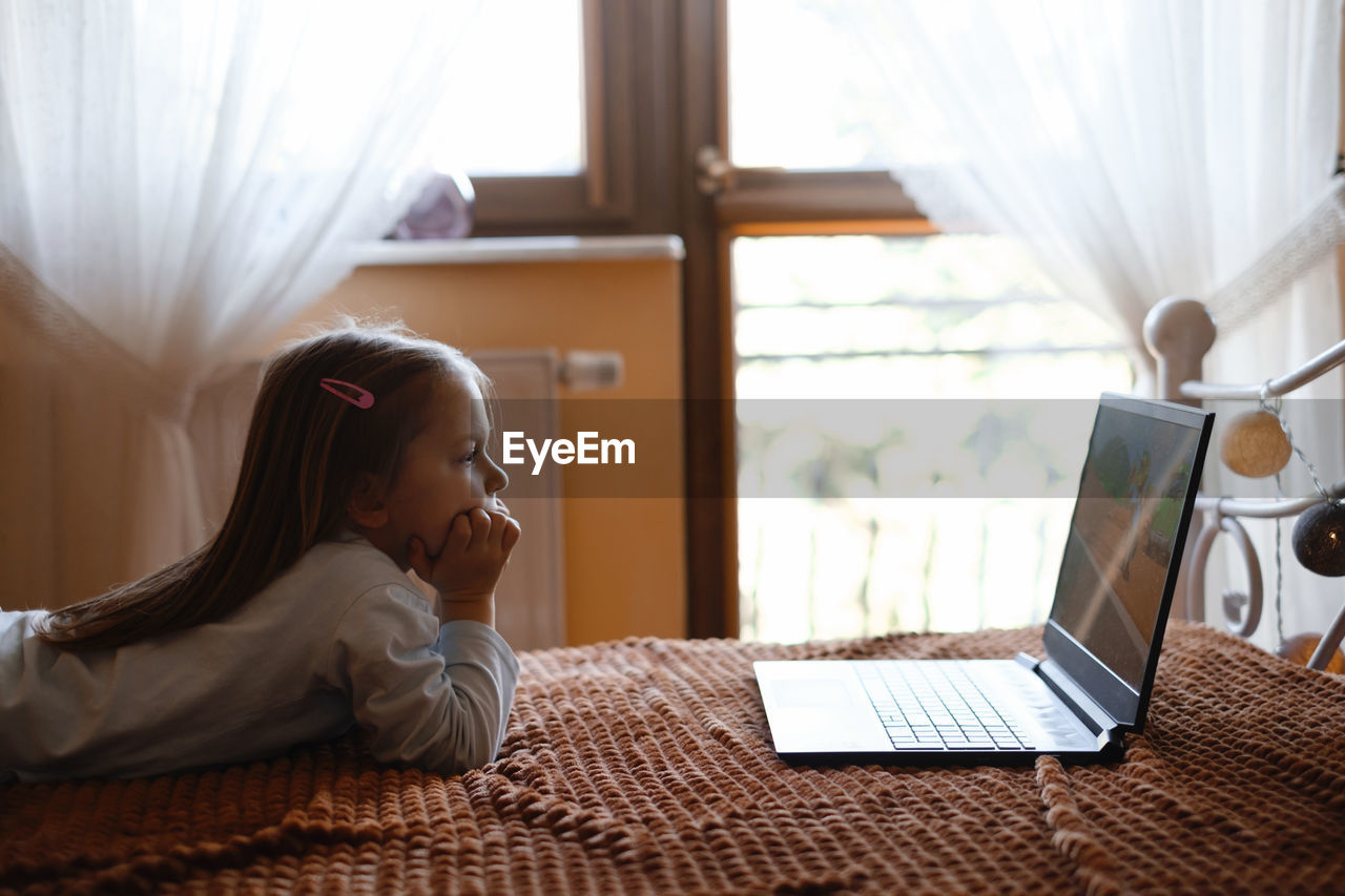 Child watching cartoons on laptop. serious kid with technology at home on bed spending time on-line