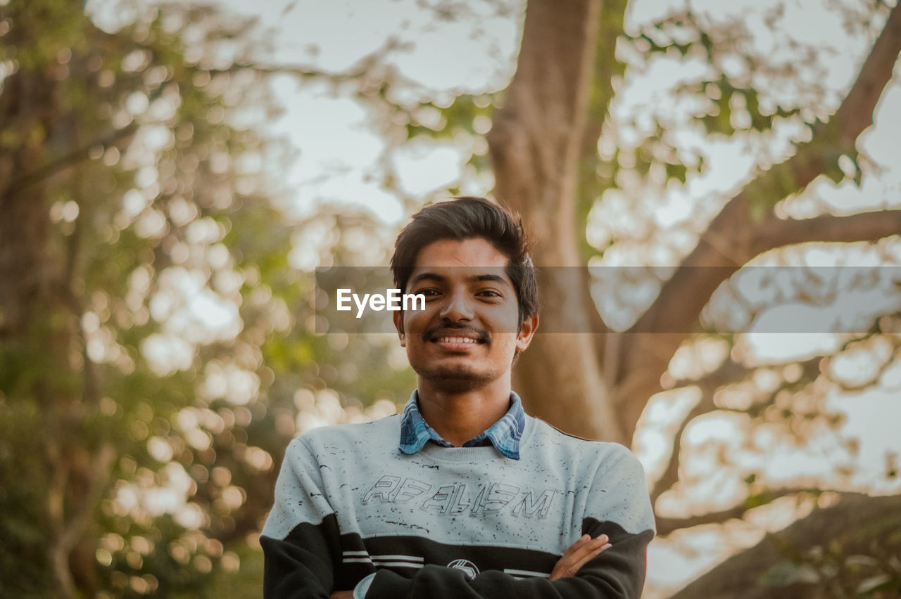 Portrait of young man standing against trees