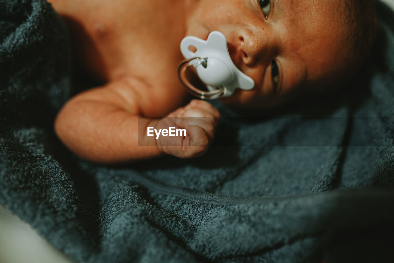 High angle view of baby boy with pacifier lying on bed at home