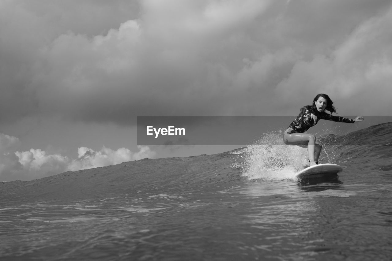 Woman with funny face surfing in the sea against sky