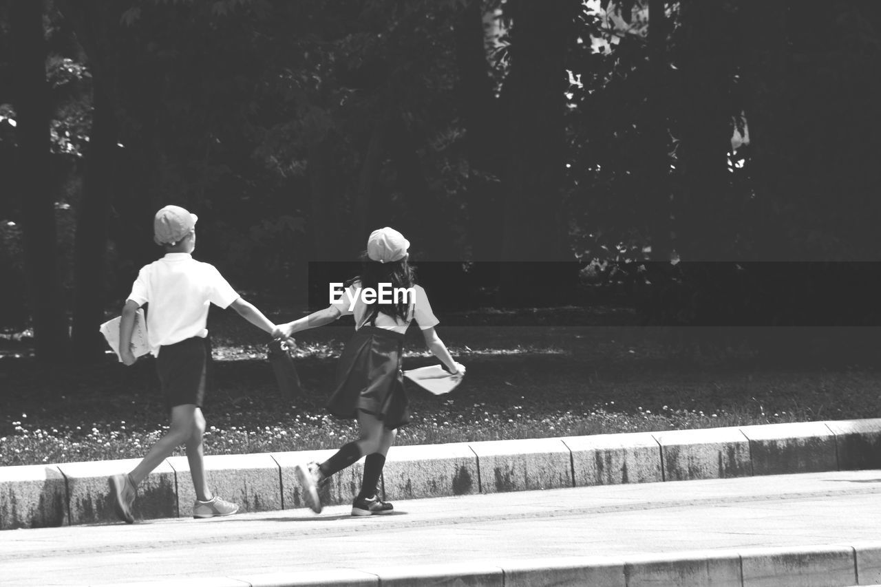 Rear view of siblings holding hands running on street during sunny day