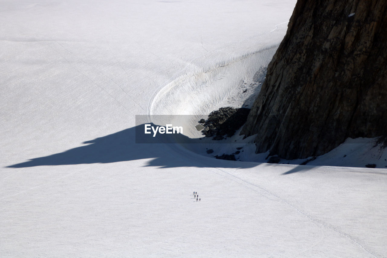 High angle view of mountain reflecting its shadow on the glacier, where some people are trekking.