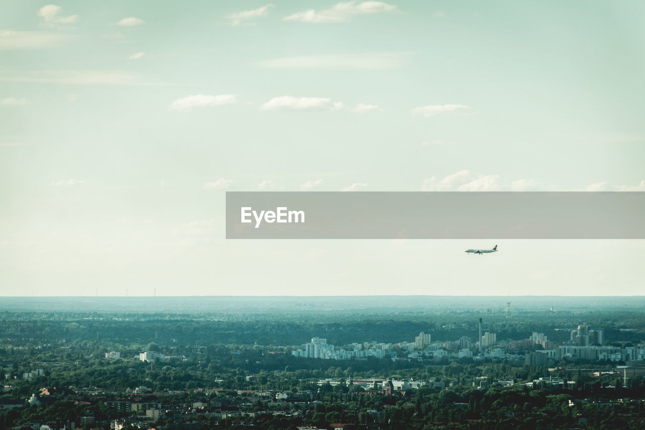 Airplane flying over cityscape against sky