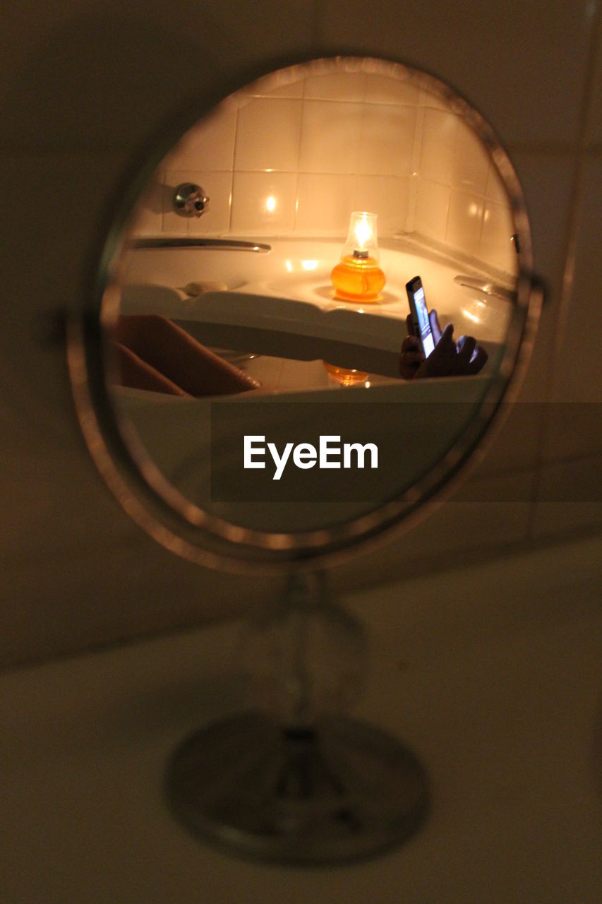 Reflection of woman using phone in bathtub on mirror