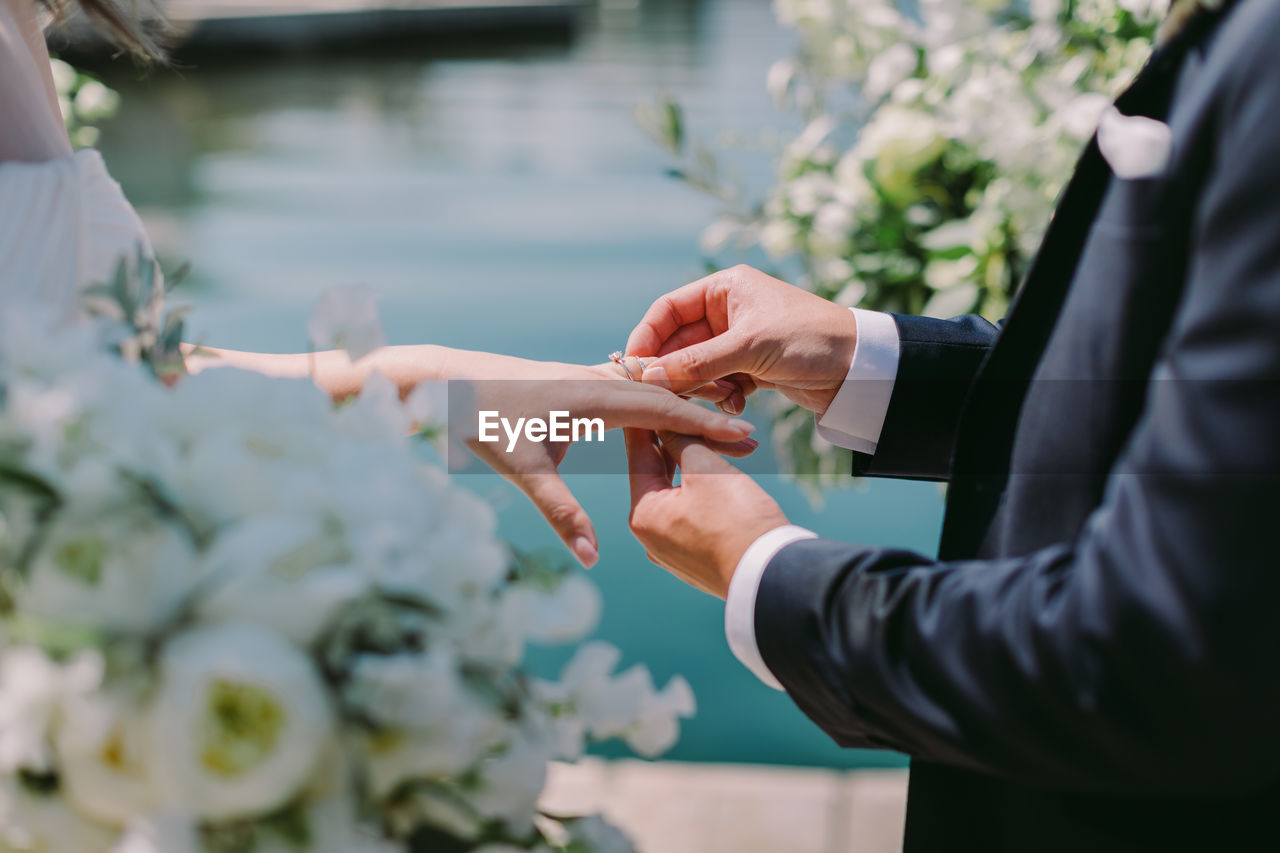 Midsection of groom putting ring on bride finger