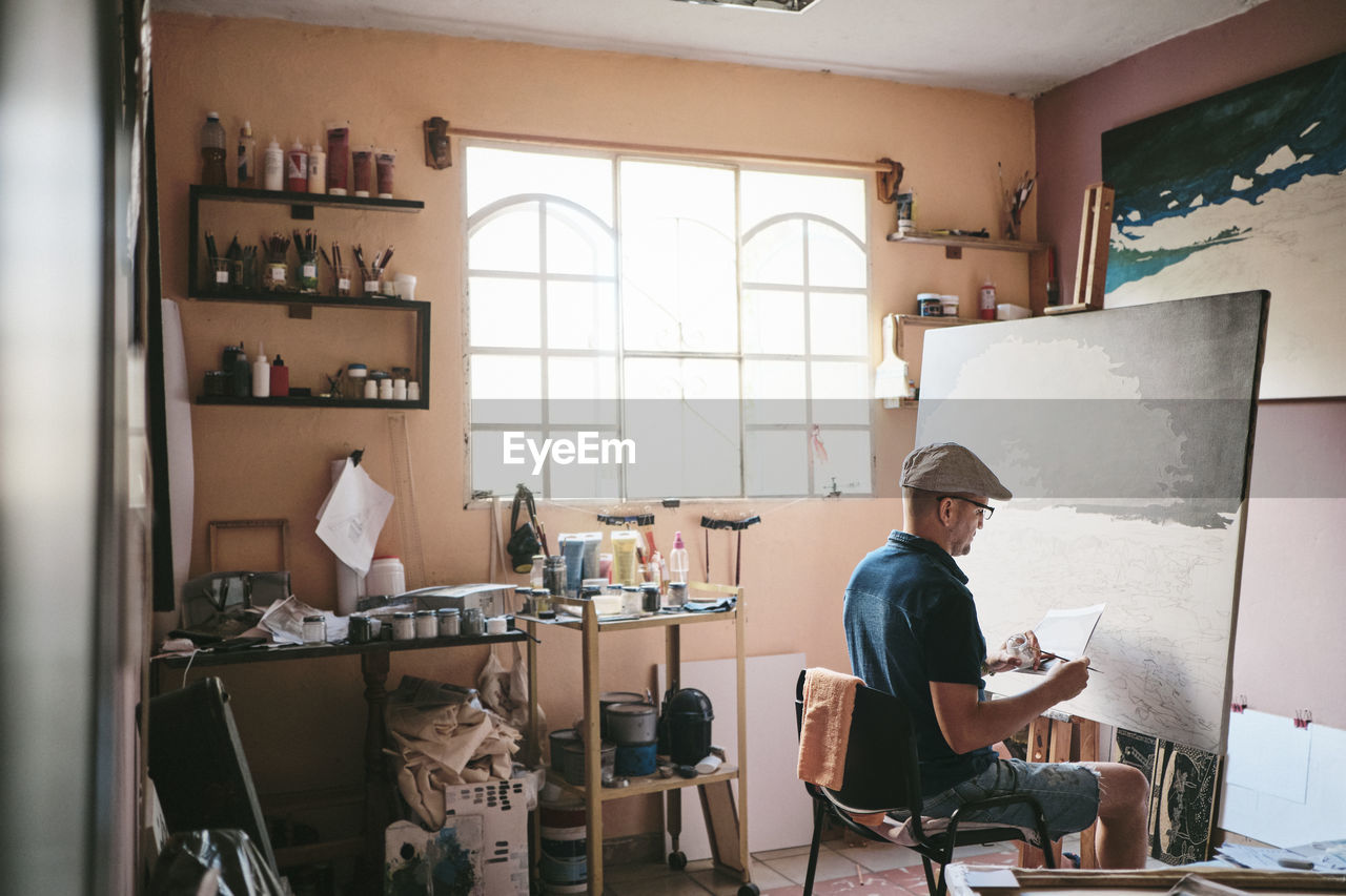 Mid adult man working as painter with brush and canvas in his studio