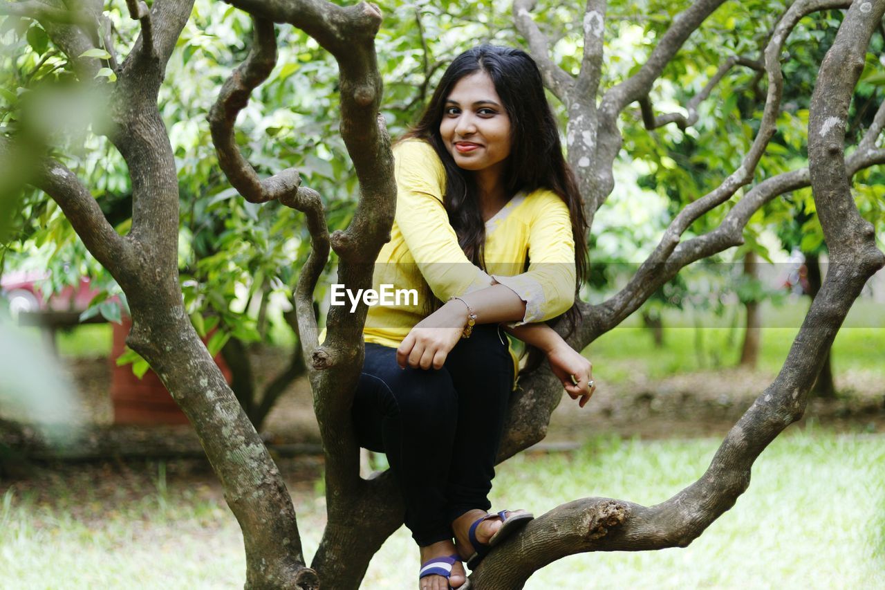 Full length portrait of young woman sitting on tree trunk