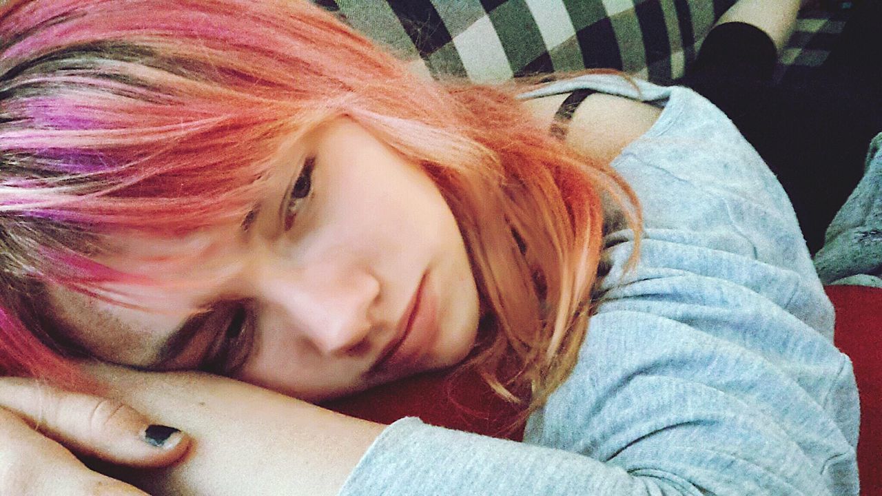 Sad teenage girl with dyed hair lying down on sofa
