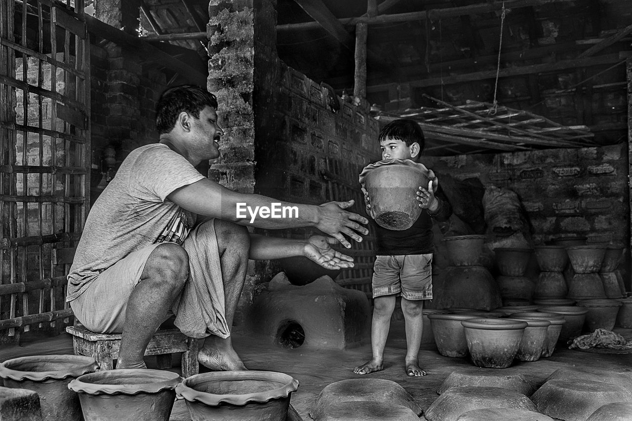 Father looking at son holding pottery in workshop
