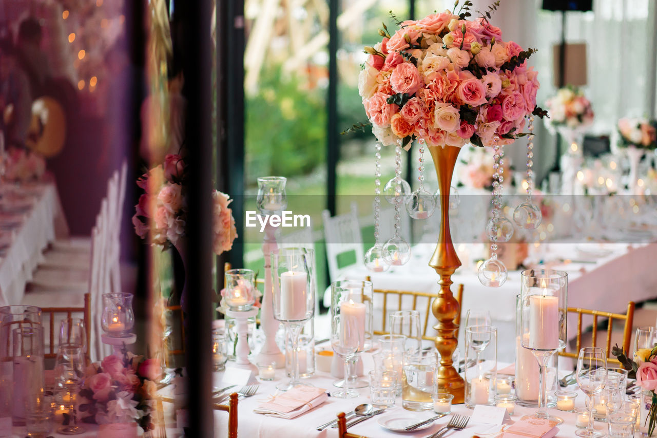 View of a beautiful table arrangement of pink roses, white candles and table cloth during a wedding