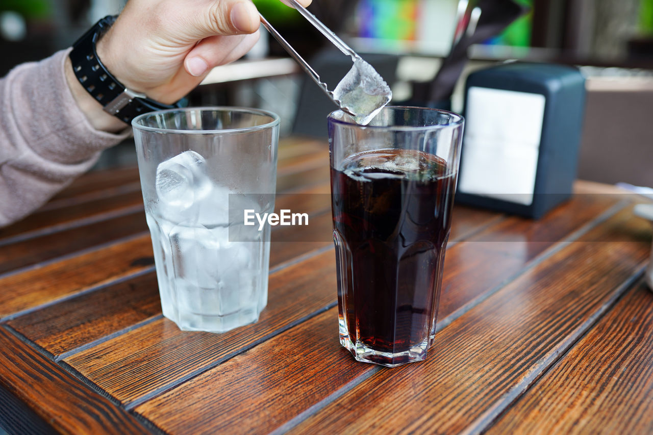 A glass of fresh ice cold lemonade on wooden table of coffee . close up of male hand,