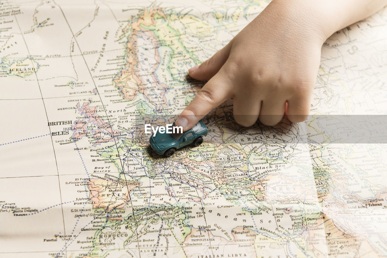 Cropped hand of child holding toy car on map