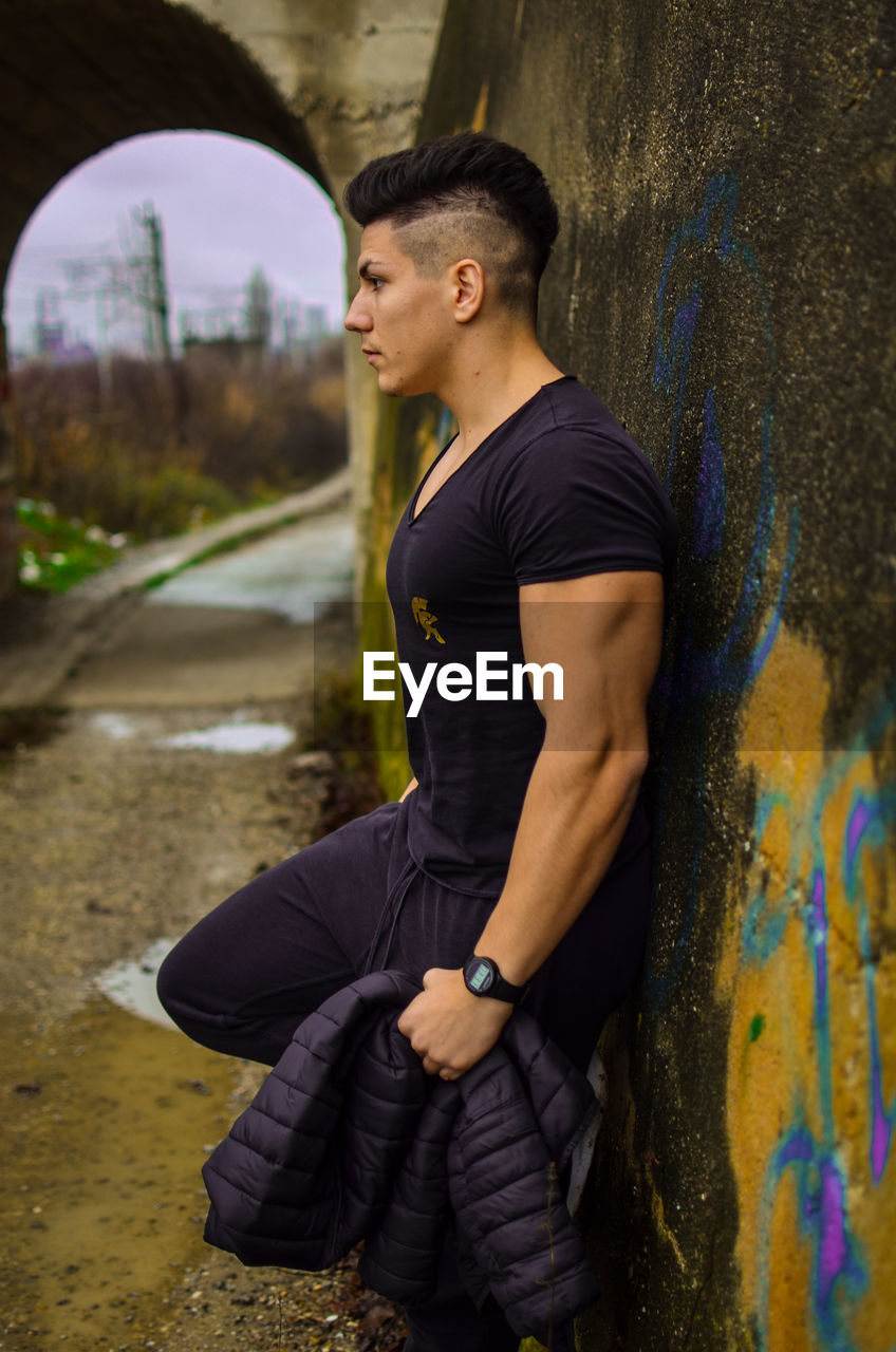 SIDE VIEW OF YOUNG MAN STANDING AGAINST BLURRED BACKGROUND