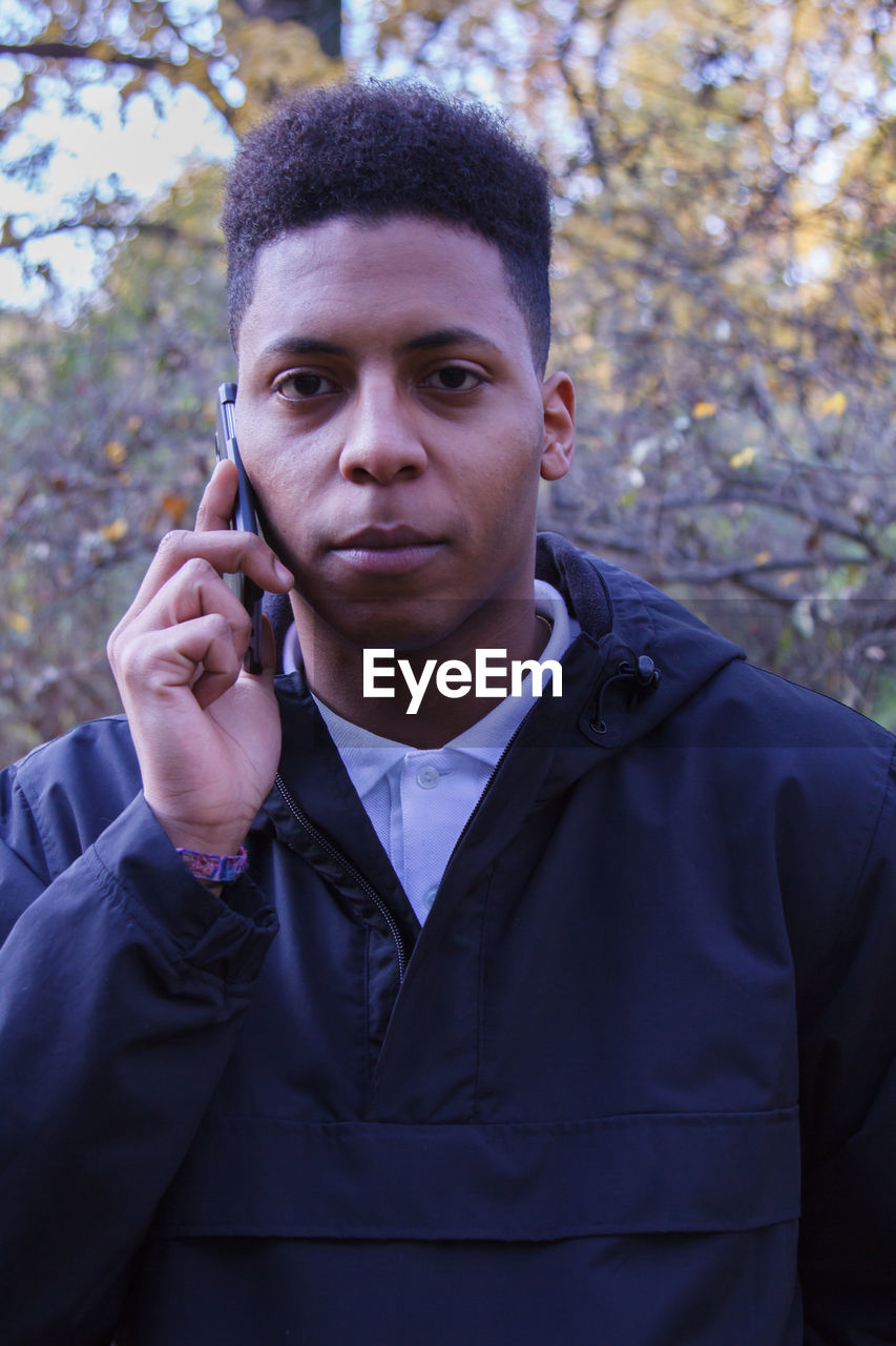 Portrait of young man talking on mobile phone while standing against trees