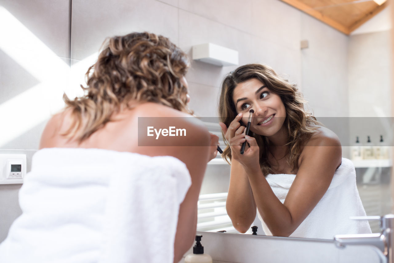 Rear view of women applying make-up standing in bathroom