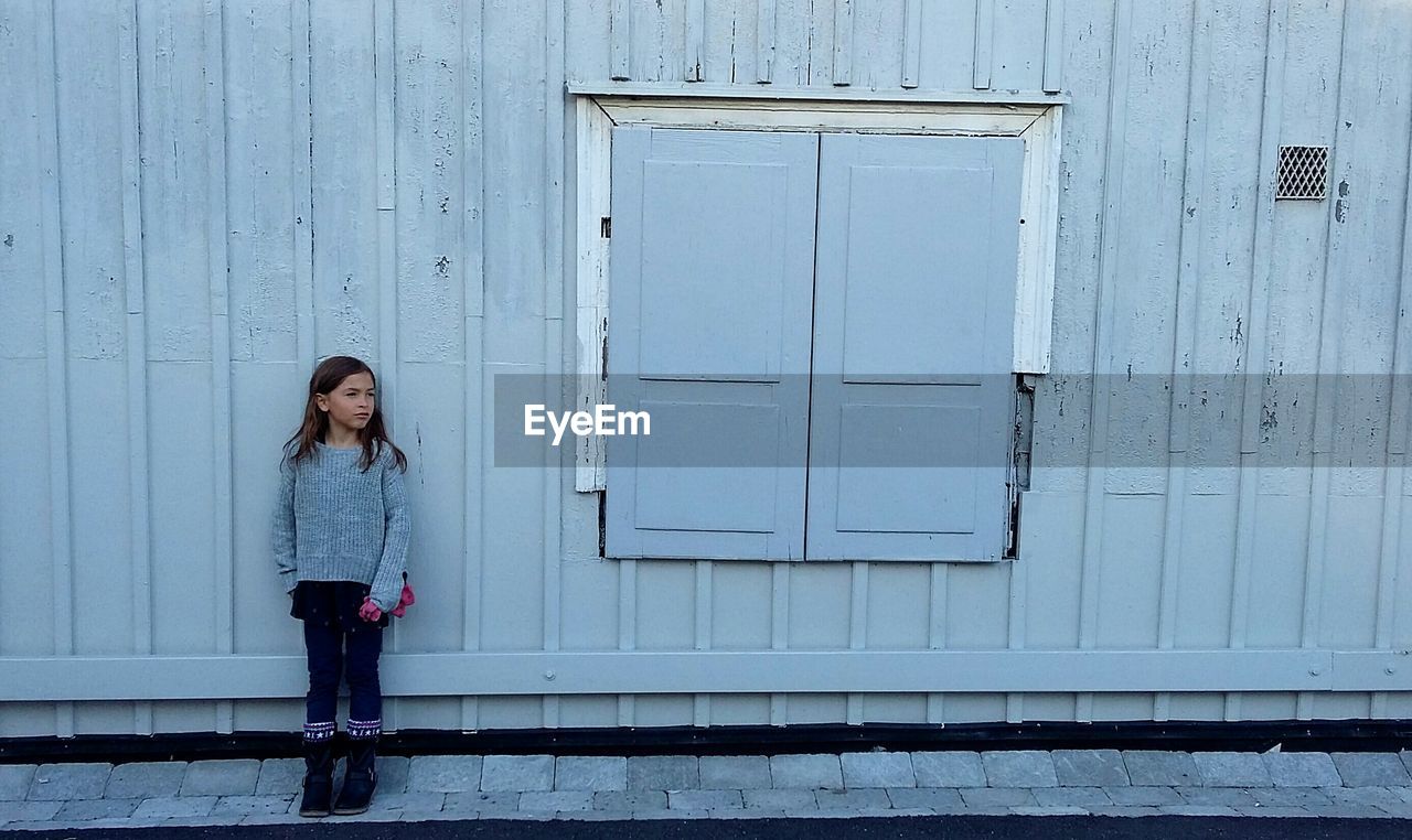Full length of girl looking away while standing against house