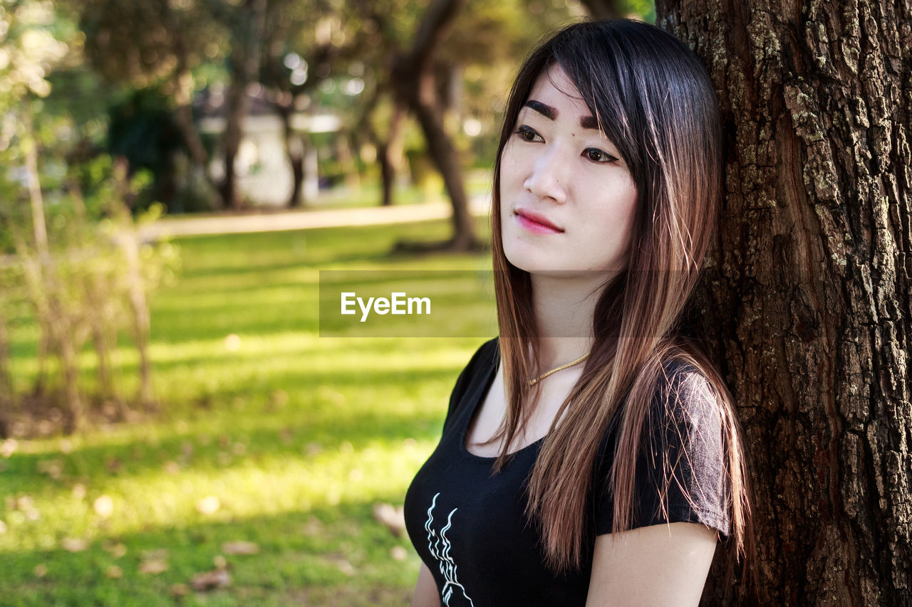 PORTRAIT OF YOUNG WOMAN WITH TREE TRUNK