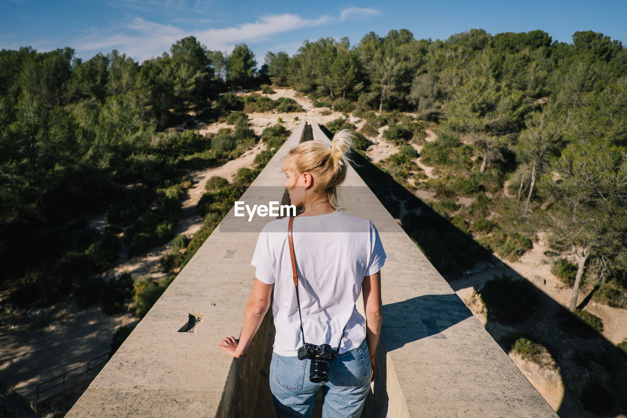 Rear view of woman standing on bridge towards forest against sky