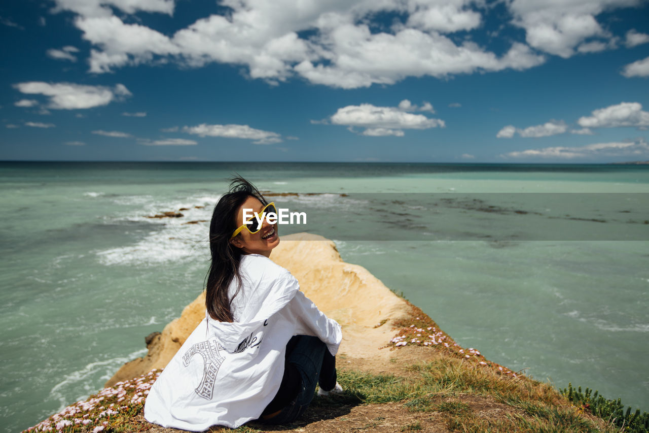 Woman sitting on shore at beach against sky