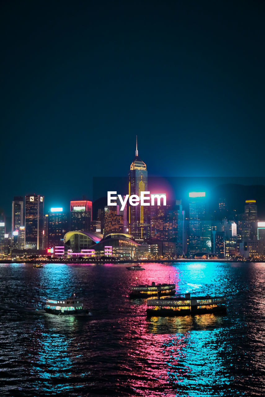 Illuminated buildings by river against sky at night