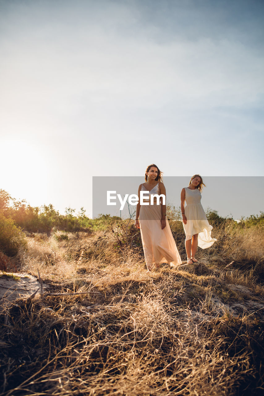 WOMAN STANDING ON FIELD AGAINST SKY