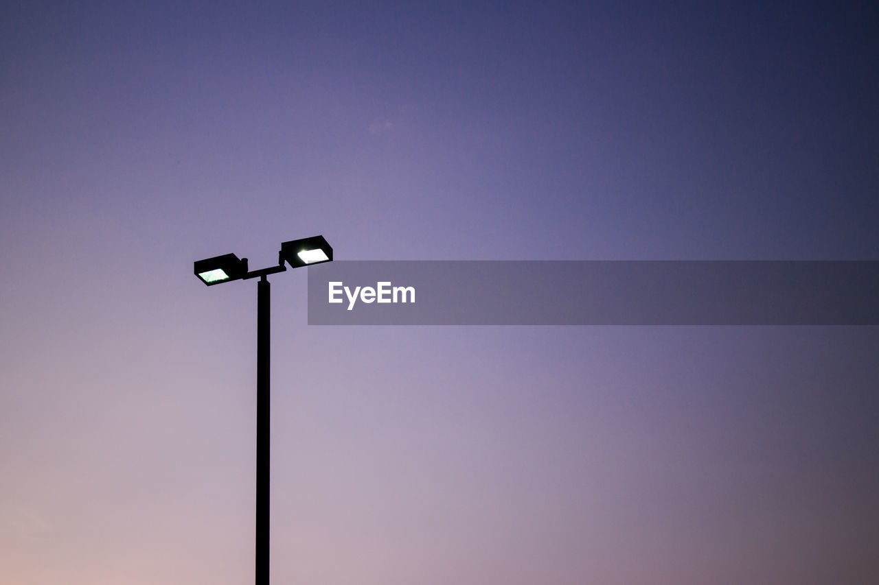 Silhouette of illuminated floodlight against sky