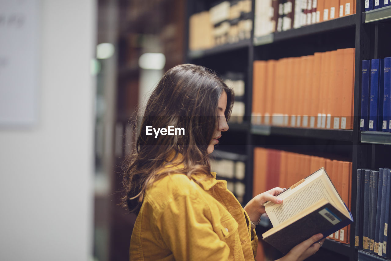 Side view of young woman reading book at library