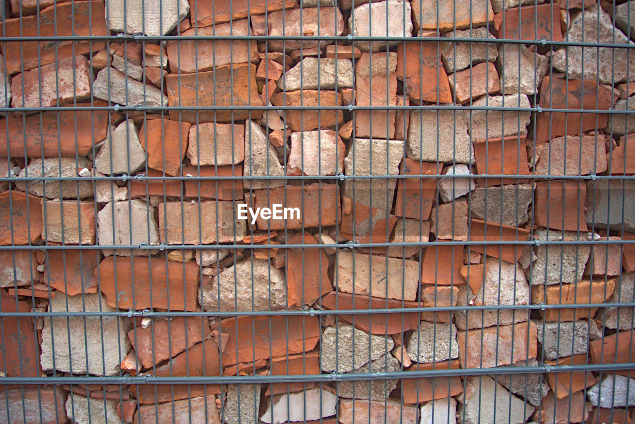 A loose brick wall kept in place by a metal fence 